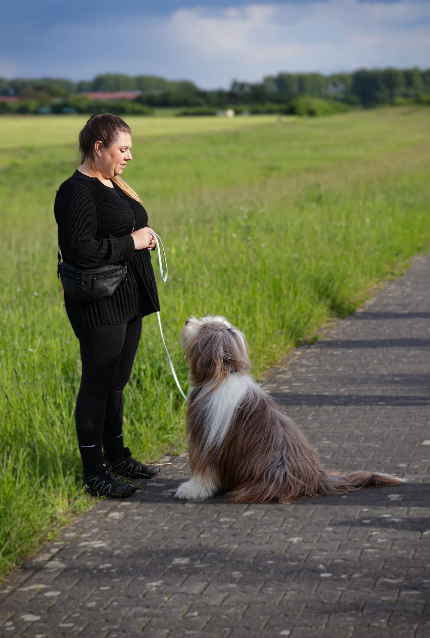Laura sitzt mit ihrem Bearded Collie auf einem Weg