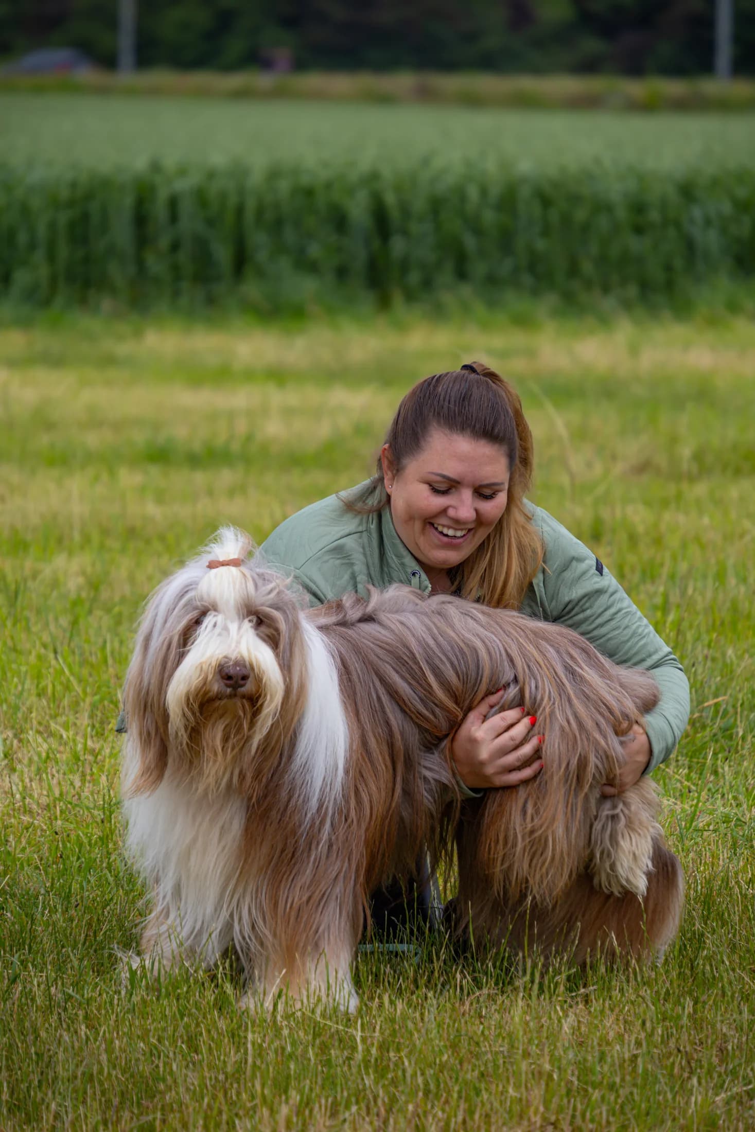 Laura kniet neben ihrem Bearded Collie auf einer grünen Wiese